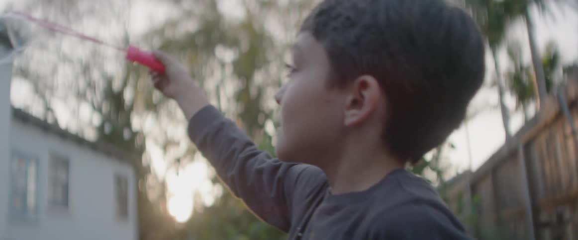 A boy is blowing bubbles in a backyard at dusk