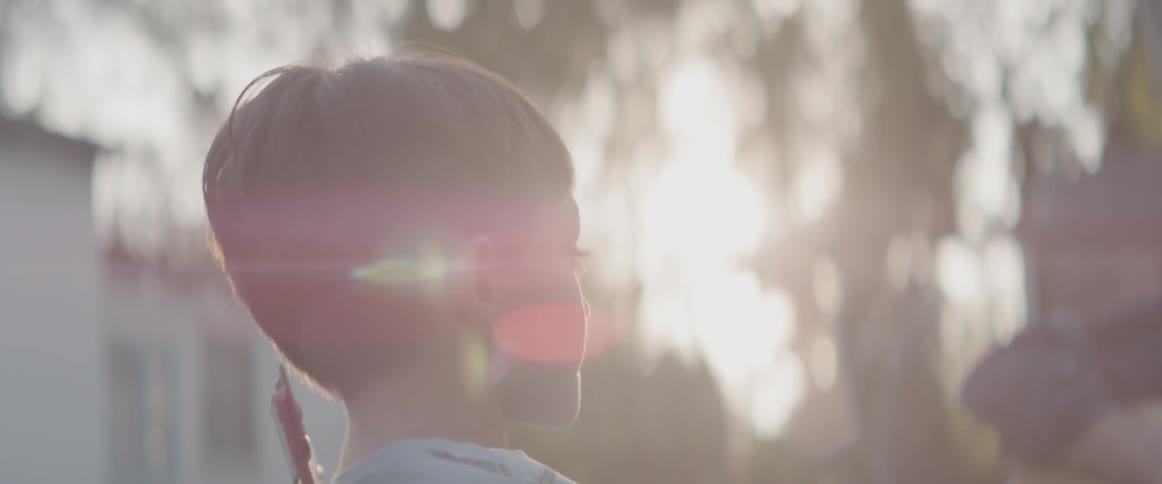 A boy is watching his father play guitar outside in daylight