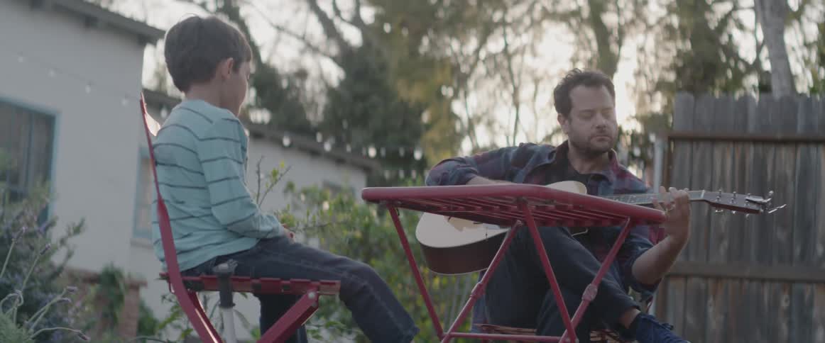 A man plays guitar on a patio with a small boy