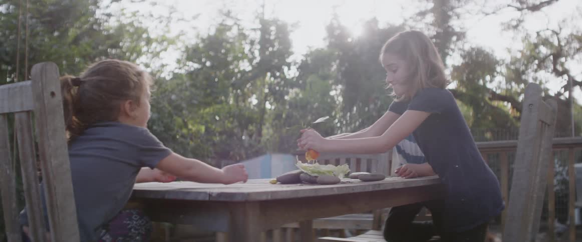 Child squeezes liquid onto a pile of vegetables on a table outside