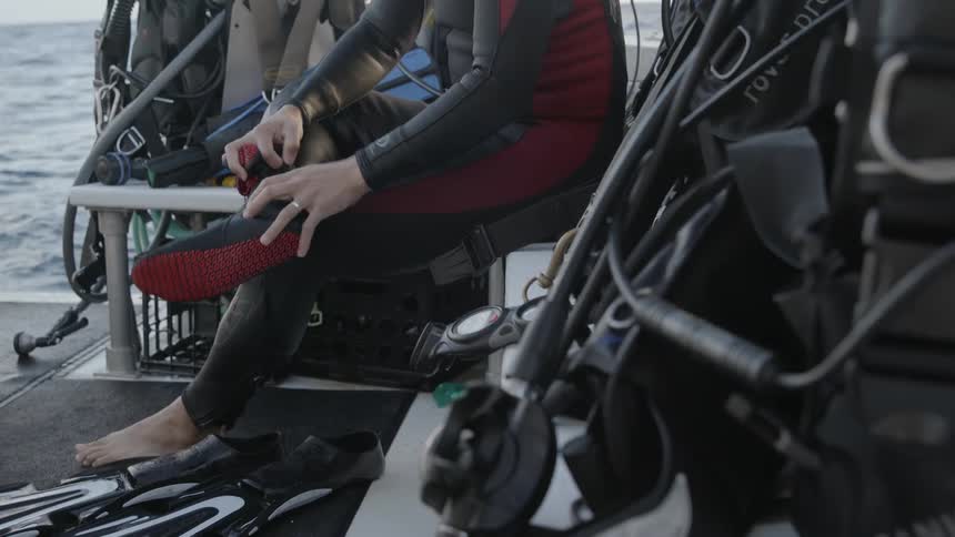 Person sitting on a boat takes off scuba gear