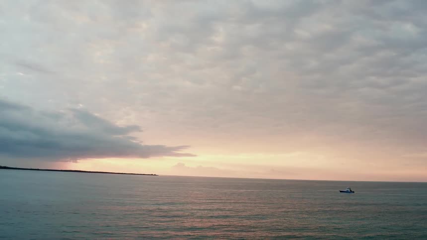A boat sails on an ocean at sunset