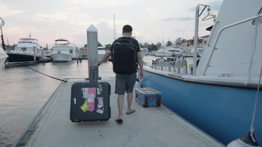 Man pulling a suitcase walks on a dock in between two boats and boards one