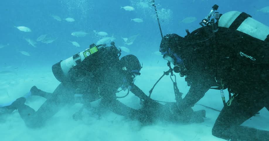 Two divers attach something to the bottom of the water