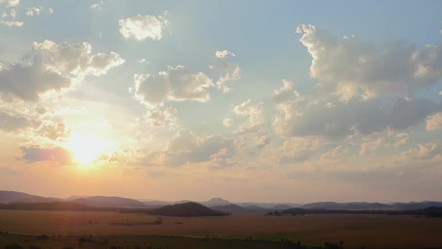 The sun is peeking through clouds as it rises over a prairie