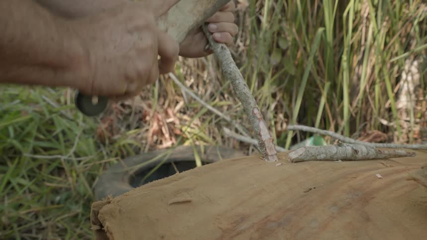 Person uses a machete to chop at a stick of wood