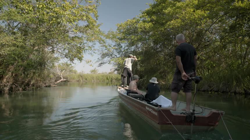 People moving along a small river lined with trees on a small boat