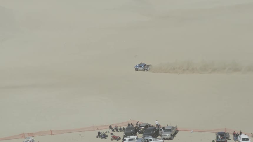 Vehicle moving across the sand as people watch