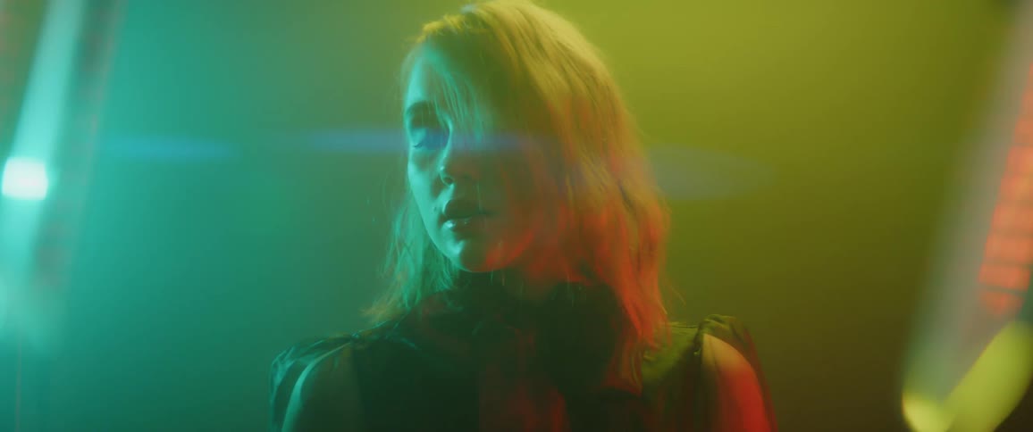 A woman stands in a foggy room with colorful lights