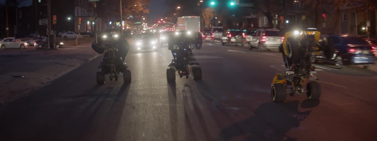 Two four wheelers drive down a city road at night doing wheelies