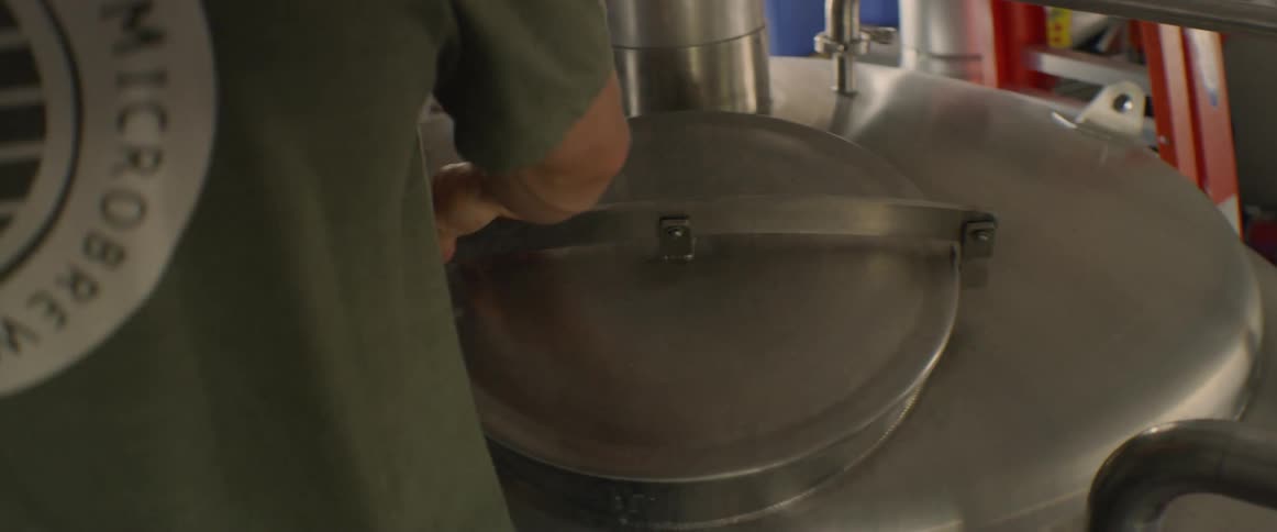 A man climbs up a ladder and opens a steel vat