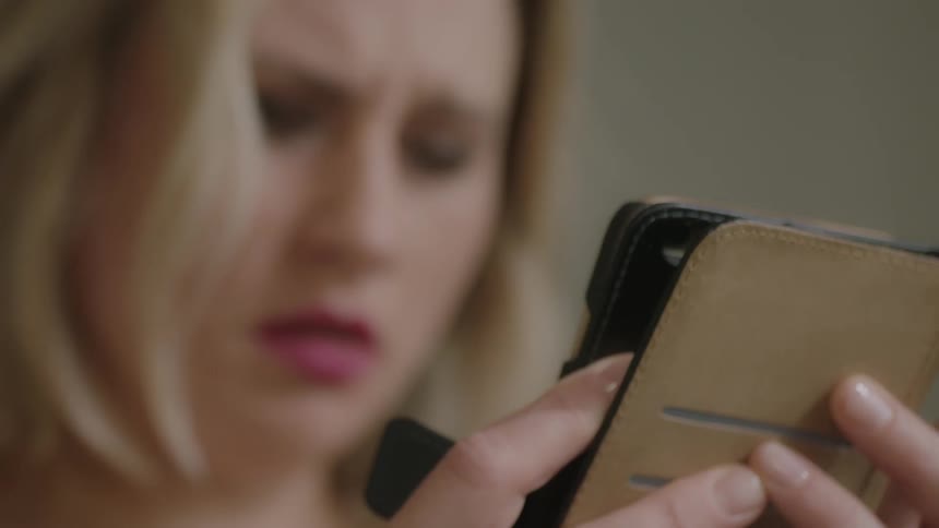 A woman is frowning as she holds her cellphone inside in daylight