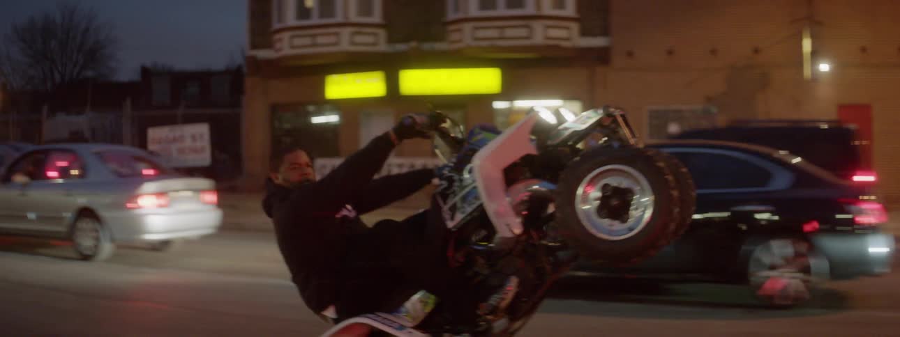 Man does a wheelie as he rides a 4 wheeler down a street