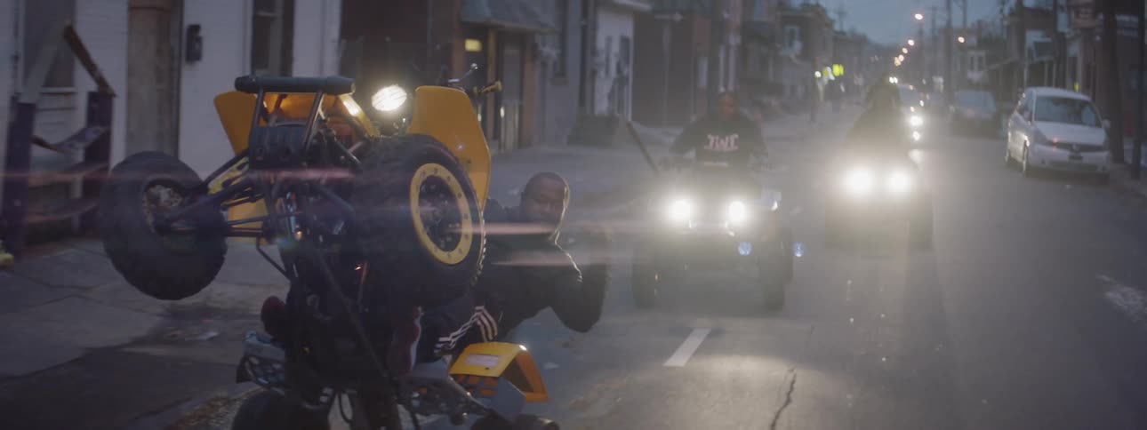 A man does a wheelie on a four wheeler as he travels down the street