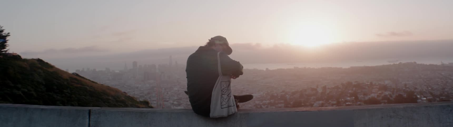 A man sits on the side of the road by a cliff