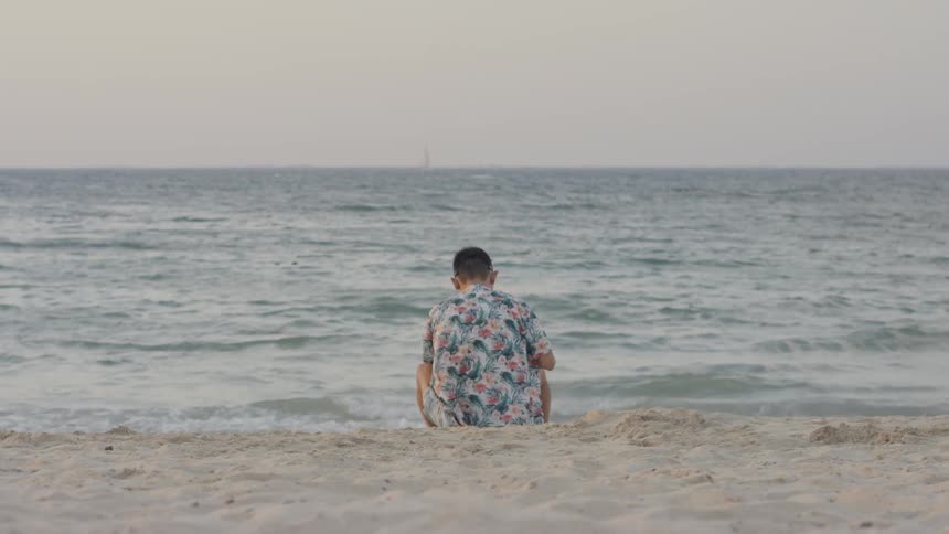 Man sits on the beach looking down