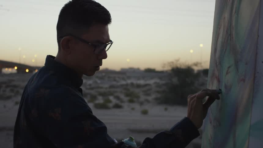 An artists is creating an artwork on canvas outside at dusk