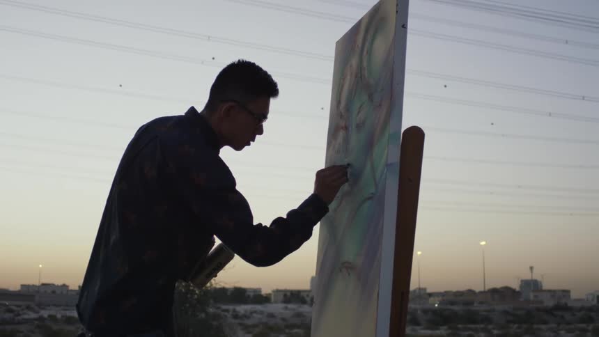 A man is drawing in the desert at sunset