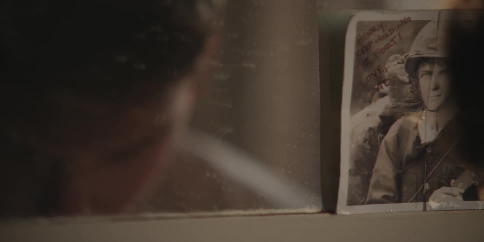 The reflection of a young man in a mirror that has an old photograph of a soldiers tucked into the corner