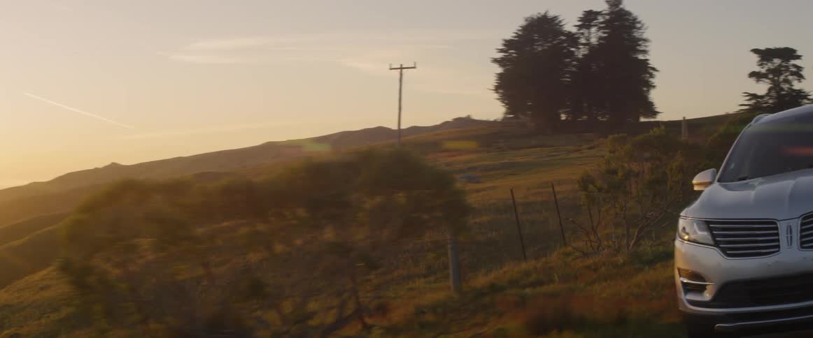 A person drives past the green hills at sunset