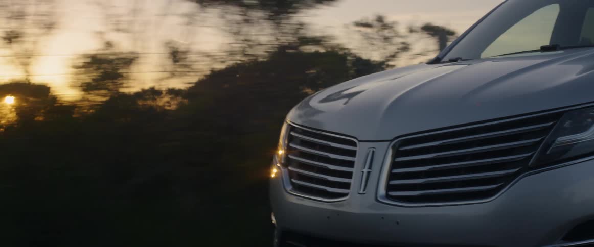 Vehicle drives down a tree lined road at sunset