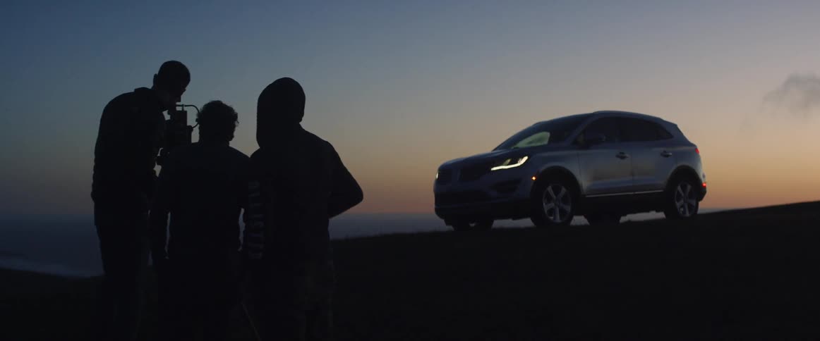 People stand by as an automobile is recorded on the hill