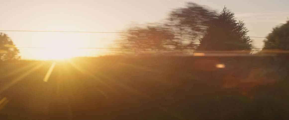 Vehicle drives down a country road at sunset
