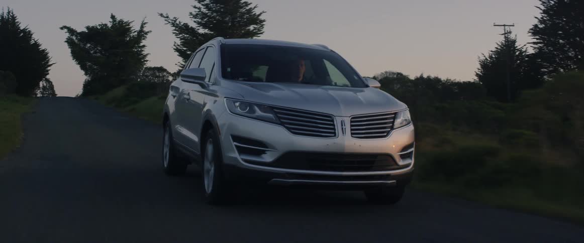 Silver car travels down a country road next to trees and fields