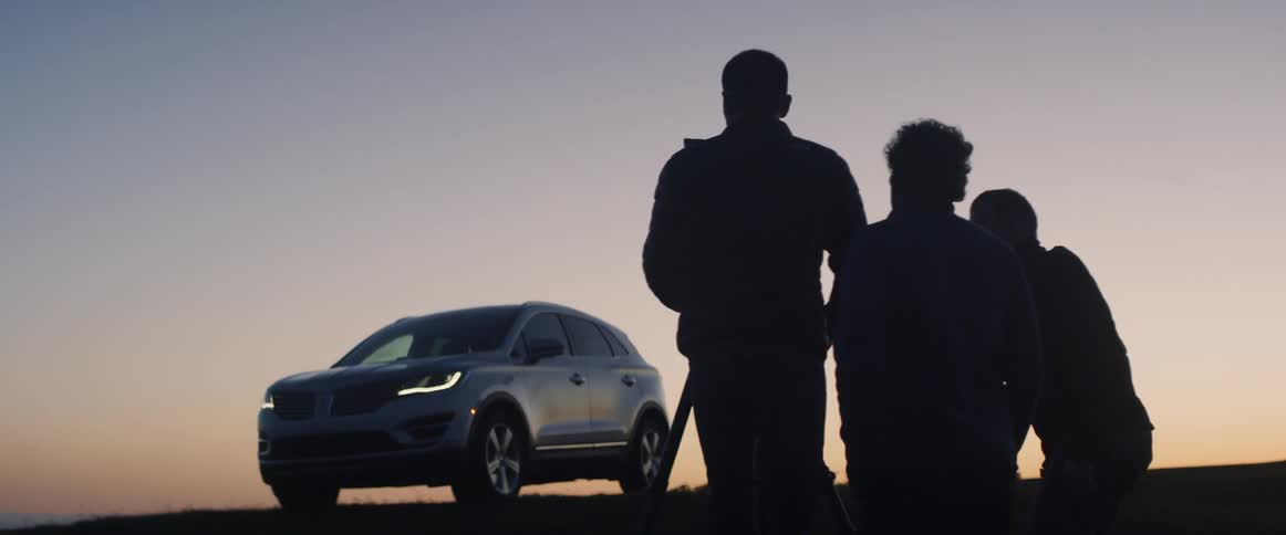 Two men film an suv at sunset