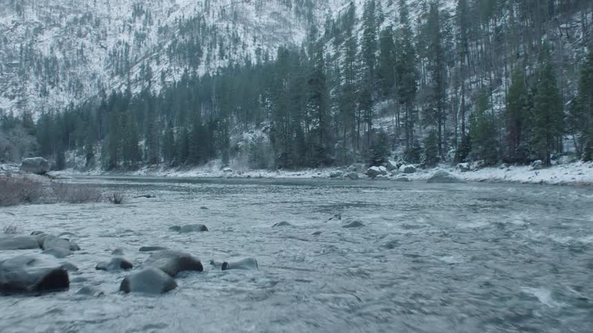 Skimming low above icy water in a mountain river valley