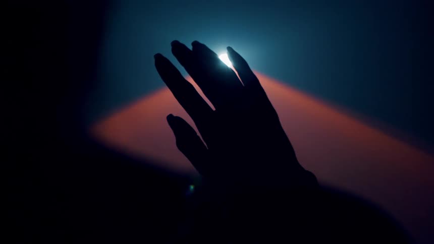 A woman's hand is reaching up into a beaming light