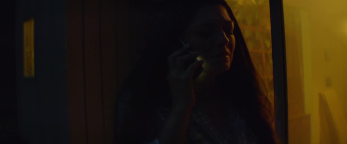 A woman is standing outside a home at night using a cellphone