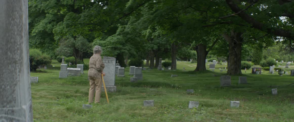 Woman holding a can looks at a gravestone in a cemetery