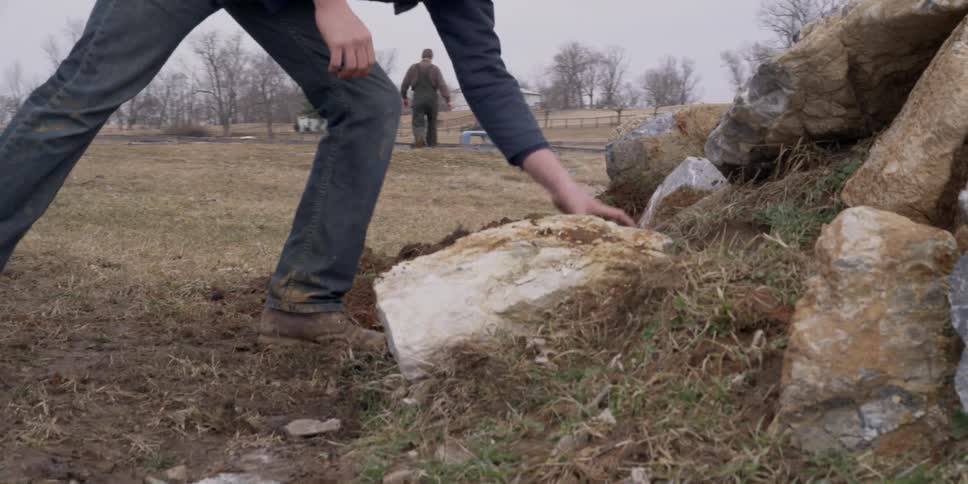 A man removes rocks and digs on dirt on a farm