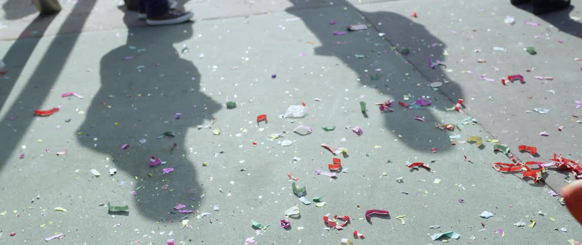 People walk on a sidewalk with confetti on the ground