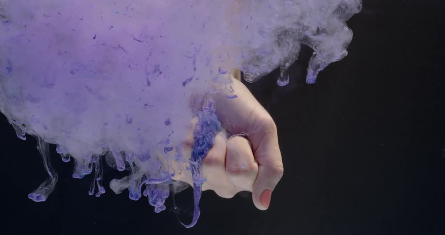 A cloud of purple colored dye is billowing from a hand underwater