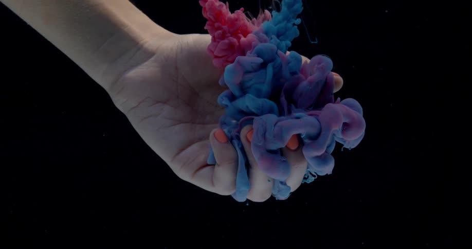 Billowing clouds of dye are falling into a woman's hand held underwater