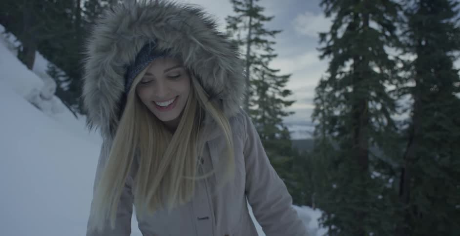 A woman is smiling as she walks on a snow-covered hillside in daylight