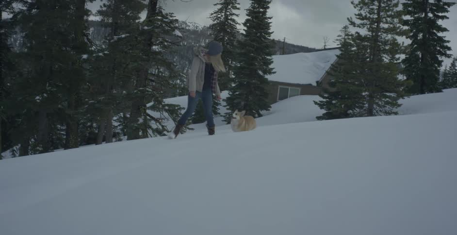 A woman and her corgi walk in the snow