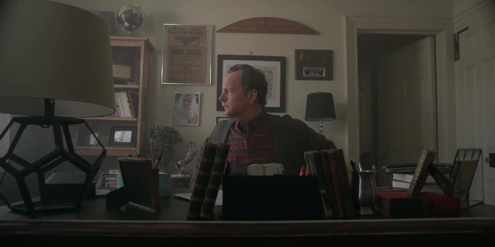Man sits at a desk then gets up to look out the window