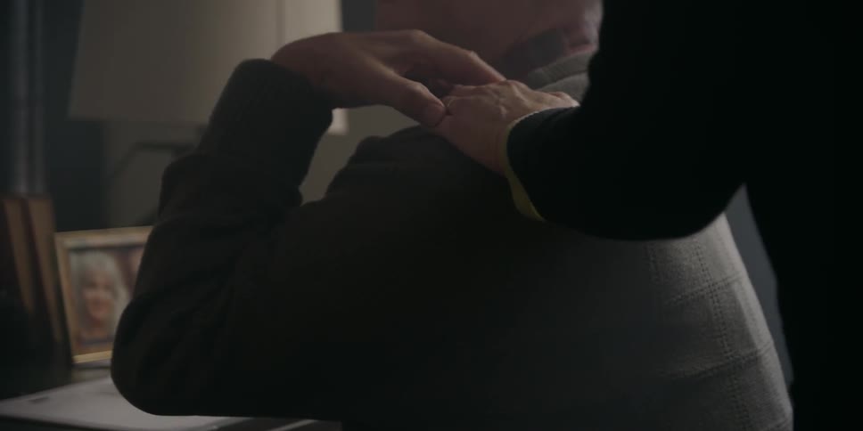 Woman with black sweater touches mans shoulders sitting at a desk at home