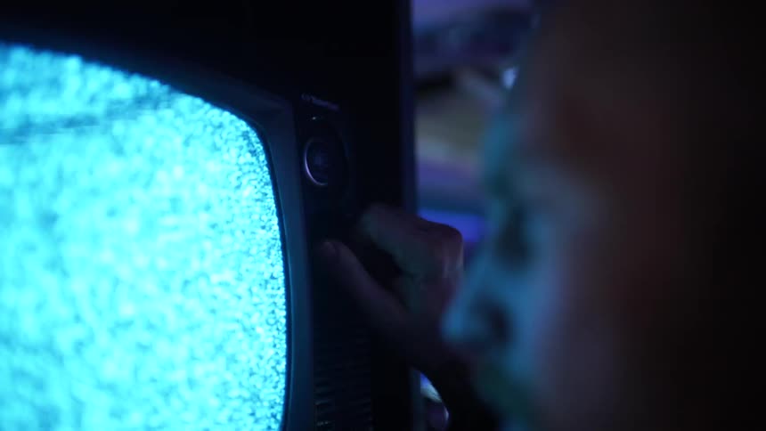 A man adjusts a knob on a tv playing static