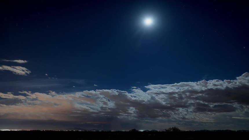 A thunderstorm is filmed in the distance with the moon above the clouds