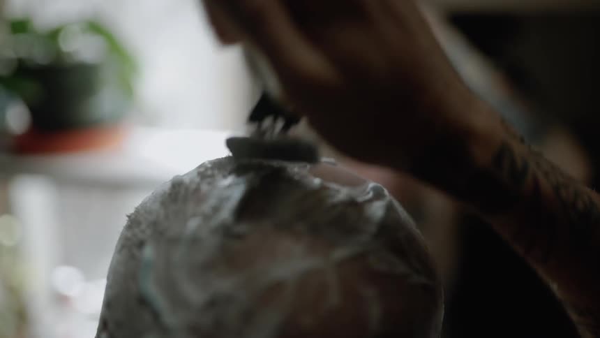 Man shaves another man's head with a razor