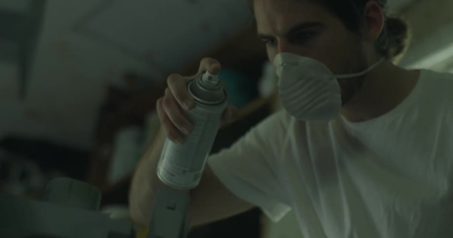 A man is spray painting his project wearing a mask