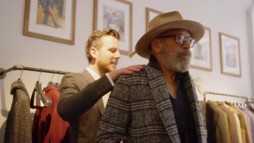 A shop worker helps a man try on a jacket