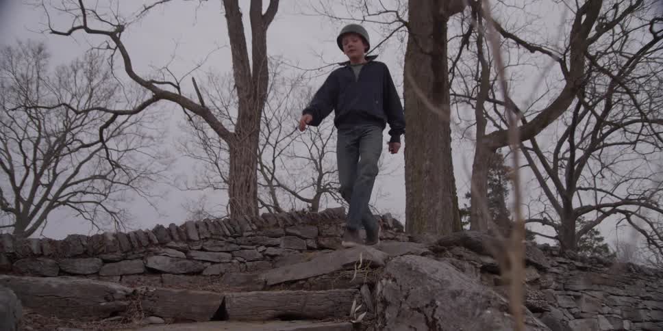 A young white kid with a coat and hat runs over a stone staircase outdoors