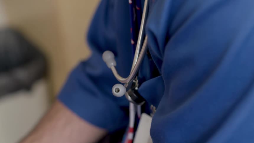 A medical professional sitting in a room with a stethoscope around their neck