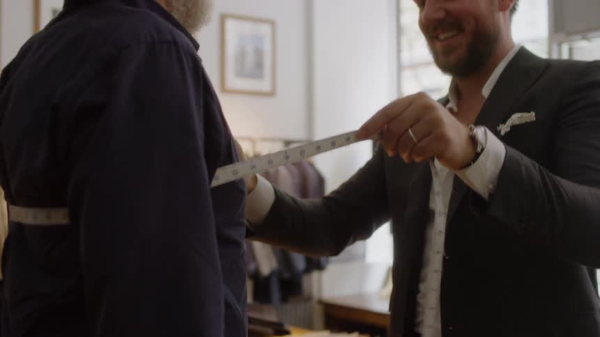 A tailor is measuring a man's chest in a suit shop in daylight