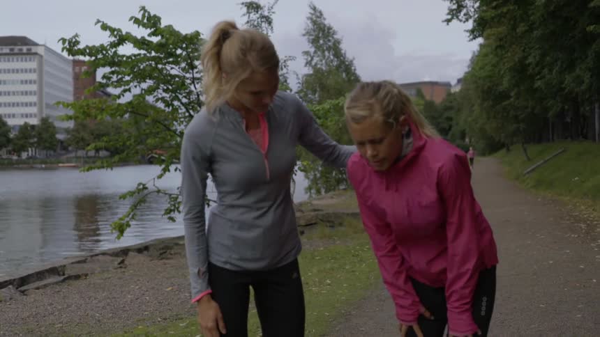 A supportive runner checks on her exhausted fitness partner breathing heavily outside town.